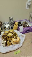 Photo showing various owl figurines in a white plastic bag, showing a mix of yellow, white, and natural tones with different sizes and finishes.