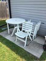 White round resin patio table with paint splatter and leaf, near siding and grass.