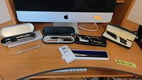 Overview of all items including 5 pens in presentation cases, 1 loose silver pen, and a metal letter opener on a desk.