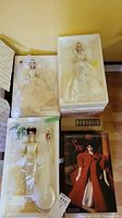 Four boxed porcelain dolls arranged in two rows on floor: three bridal dolls and one in red packaging