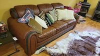 Full view of brown leather sofa with decorative pillows and cowhide rug