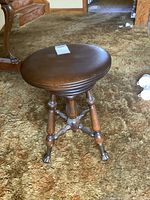 Front view of antique wooden piano stool on carpet, showing round seat and four legs.