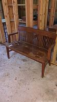 Front view of wooden bench with slatted back, arms, and seat in barn setting