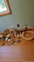 Wide view of all items arranged on floor including stained glass birds, fabric prints, candleholders, vases, jug, wood giraffe, wicker basket, and round woven tray.