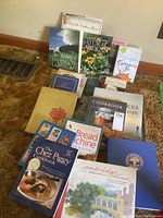 Books arranged on carpet floor in mixed pile showing titles related to cookbooks, gardening books, and regional subjects