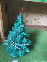 Front angle view of the ceramic Christmas tree showing multicolored lights, electrical cord, and red star topper with chip.