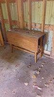 Table folded with both leaves down, showing top and side profile against barn wall.