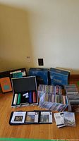 Wide view showing two blue Trivial Pursuit boxes, black poker chip case with chips in four colors, stacks of CDs in jewel cases, crossword puzzle booklet with orange cover partially visible.