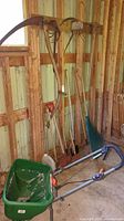 Photo of garden tools including the seed spreader and various long-handled tools hung on a wooden wall in a barn