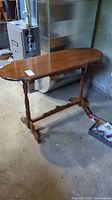 Full view of the wooden hall table showing the oval top, turned legs, and support beam. Scratches visible on the tabletop.