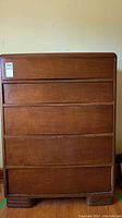 Frontal view of the highboy dresser showing five handleless drawers and wood surface with scratches.