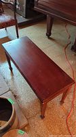 Side view of wood piano bench showing flat rectangular top, legs and storage feature beneath the seat.