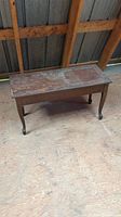 View of top and side of rectangular wooden piano/organ bench showing worn finish and chipped edges