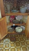 Cabinet shelf with mixed glass and ceramic serviceware items: multiple glass bowls and plates of various sizes, ceramic mug, divided dish, and some smaller items