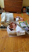 White sewing machine with hard case, wooden meter stick, fabric swatch, lidded tote with linens, and shoebox of sewing supplies on wooden floor.
