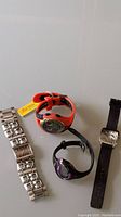 Four watches displayed: one with stainless steel band, one red resin band watch with tag, one black and purple resin watch, one black leather band watch