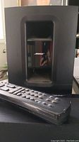 Close-up image of Bose Cinemate 1SR subwoofer and remote control device in front of it.