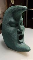 Front and side view of the ceramic sleepy moon figurine showing textured surface and sculpted closed eyes and open mouth.