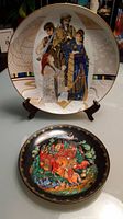 Two vintage collector plates shown together, one larger with biblical figures, the other smaller with colorful horse and knight scene.