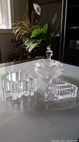 Photo showing the three crystal pieces: pinwheel candy dish with lid, star-shaped dish, and triangular dish with lid on reflective surface with background plants.