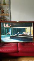 Full view of framed glass art print showing diner scene on red sofa backdrop