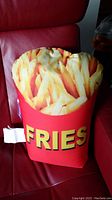 Full view of graphic French fries pillow sitting on red chair showing overall shape, colors, and text.