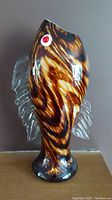Front and side view of fish-shaped glass vase showing brown and amber swirled pattern with clear fins and red eyes.