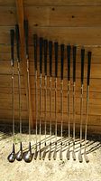 Full set of 11 golf clubs including irons and woods leaning against wood wall outdoors