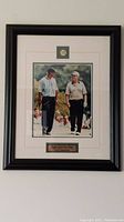 Full view of the framed photo showing Tiger Woods and Bear Bryant walking on a golf course, the Masters Augusta pin above, and frame details.