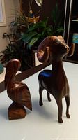Photo showing two solid wood carvings: a pelican and a big horn ram. Both are dark wood with carved details and the ram has some visible scratches.