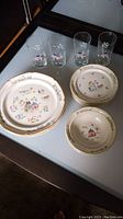 Overview of 4 large stoneware plates, smaller plates, and 4 glass drinking glasses all featuring farm and floral decor.