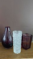 Front view showing all three vases: clear textured Ice vase, deep purple teardrop vase, and purple square Pentik vase