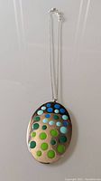 Front view of the vintage Swatch necklace showing oval pendant with blue and green circular dots, hung on a silver-tone adjustable chain.