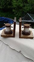Pair of vintage wooden nautical pulley bookends shown side by side on a white cloth outdoors, with greenery and a metal rack in the background.