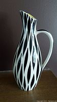 Front side view of vintage ceramic jug with black and white elongated zebra leaf pattern and curved handle