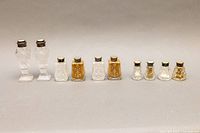 Full view showing all five pairs of salt and pepper shakers arranged by height from tallest to shortest. Various glass and crystal bodies with sterling silver and gold-tone lids.