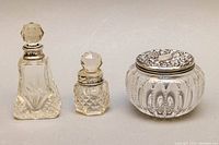 View of three items: two crystal perfume bottles with faceted stoppers and one round powder jar with a sterling silver lid