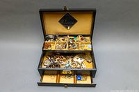 Open jewelry box showing multiple compartments filled with assorted jewelry including necklaces, rings, earrings, bracelets, and pendants.