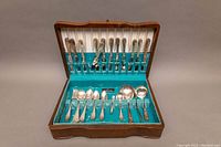 Flatware set displayed inside wooden storage chest featuring turquoise interior, includes spoons, forks, knives, and serving utensils