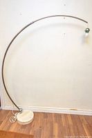 Chrome arched adjustable floor lamp with white marble round base, white power cord on floor.