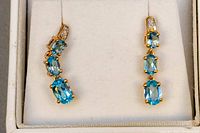 Front view of both earrings in presentation box showing three oval aquamarine stones and diamond accents