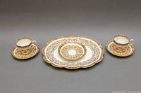 Photo of full set showing two teacups, three saucers, and scalloped platter with detailed floral and gold patterns