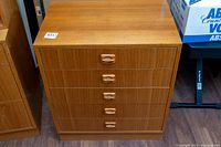 Front view of small teak dresser showing four drawers with wooden handles and wood grain finish.