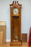 Full front view of oak case, swan neck pediment, glass door, dial and pendulum visible