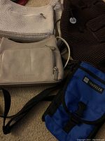 Four women's bags displayed together: brown woven The Sak backpack, white The Sak crossbody, beige leather Stone Mountain bag, blue LLBean Traveler bag.