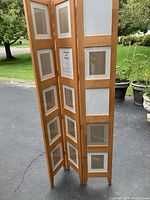 Three-panel oak room divider with picture frames slots on one side, shown outdoors on driveway against greenery background.