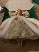 Barbie doll in its box, dressed in gold and cream gown with faux fur trim, viewed from above showing dress and hair