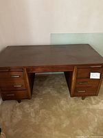 Front view of dark wood desk showing six drawers and glass top resting against the wall.