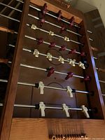 Top angle view of the foosball table showing wooden frame, metal rods, and maroon and cream colored players.