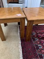 Pair of square oak side tables, positioned close together showing matching tops and legs, set on carpet and rug